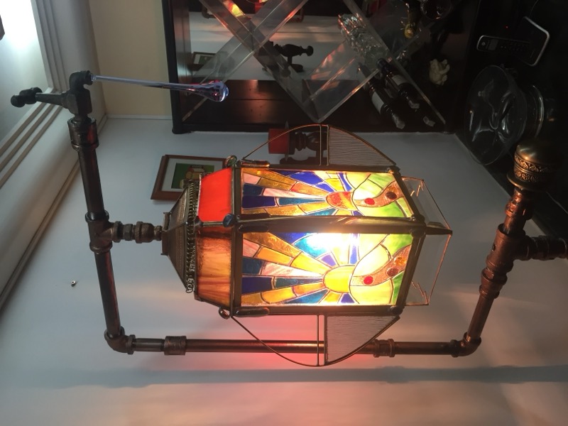 Stained glass lantern with colorful sunburst patterns on industrial pipe frame